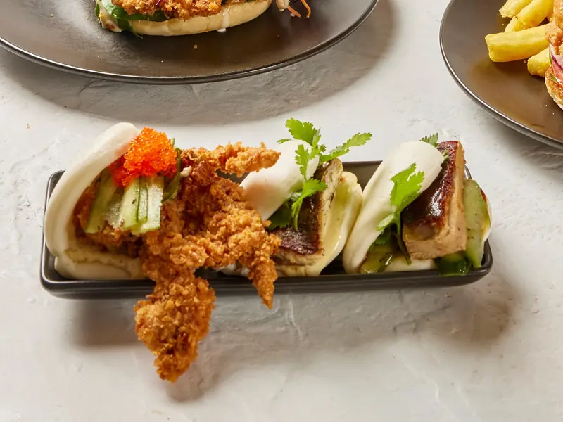 Soft-shell crab, grilled barramundi and Peking duck baos on a black tray