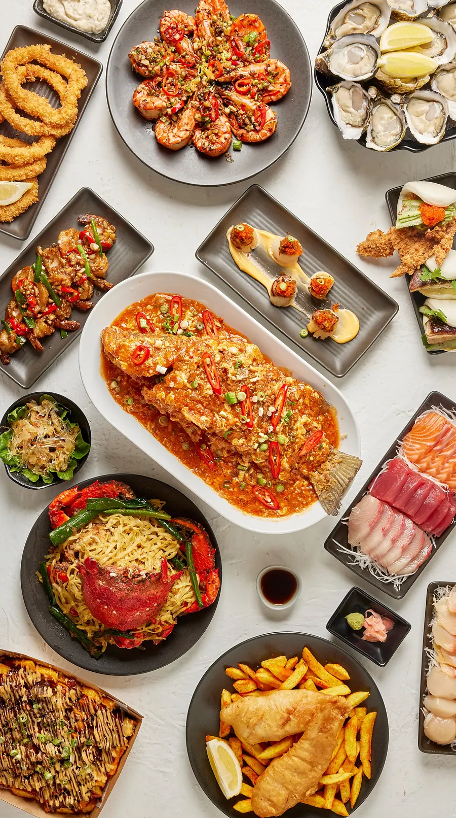 Their table: oysters, sashimi, a whole fish in chilli sauce, crab XO noodles, prawns, baos and fish and chips on white marble