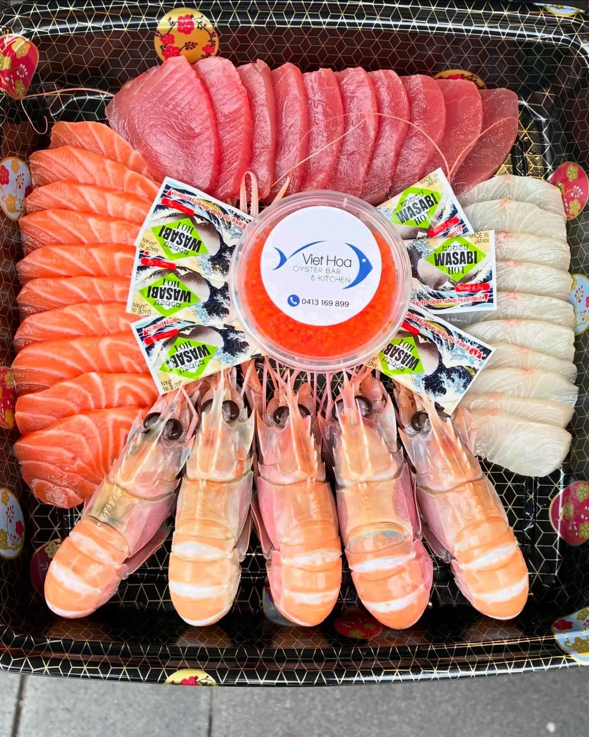 A big round sashimi platter of salmon, tuna and kingfish with king prawns and a pot of sauce